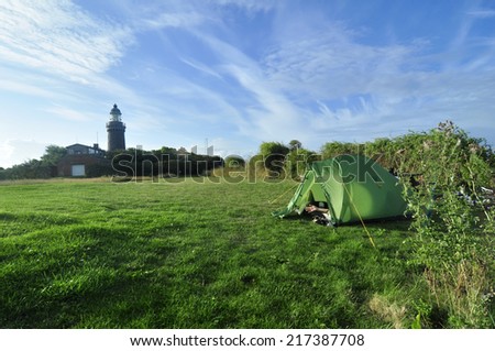 A green tent in the meadow with a lighthouse at the background with a hand saying hello in the morning