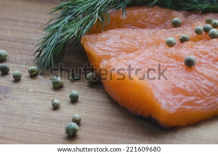 The fillet of the salmon on a wooden desk decorated with dill, lemon and green pepper