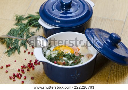 Two mini casseroles with a cooked egg with salmon inside decorated with dill and rose pepper