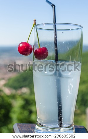 A glass of lemonade with a cherry and mountain background in a cafe