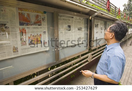 GUANGZHOU, GUANGDONG PROVINCE, CHINA - OCTOBER 13, 2006: Man reading newspapers posted in public display case on sidewalk, in the city of Guangzhou.