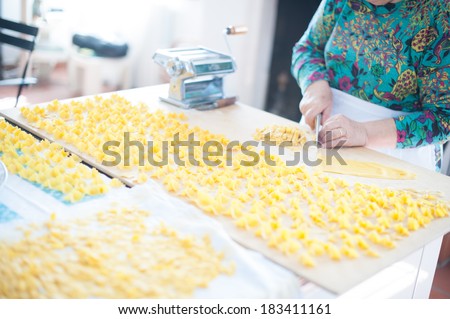 Drying home made pasta on a wooden cutting board close to a traditional pasta machine while woman\'s hands cut a rolled up fresh pasta sheet.