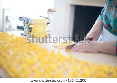 Home made fresh pasta drying on a wooden board with a traditional pasta machine and woman\'s hands cut home-made pasta in small squares.
