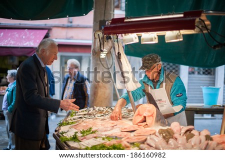 VENICE, ITALY - APRIL 1, 2014: An unidentified customer buys some fish at the fish market from an unidentified merchant, and other unidentified people around them, on April 1, 2014 in Venice, Italy.