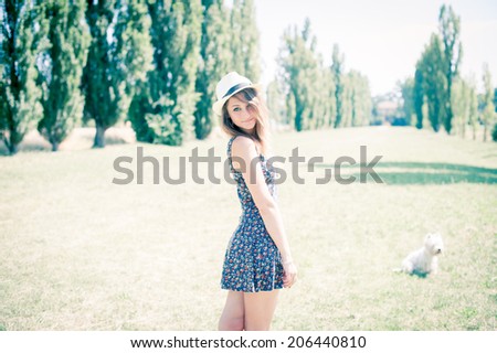 A beautiful blonde young woman enjoying spare time with her small dog in a park, with vintage-like effects.