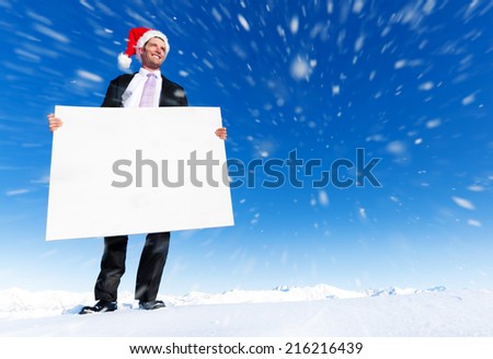 Christmas businessman holding blank placard on top of a mountain.