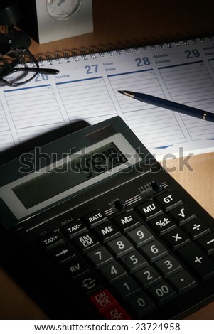 Date book on desk with calculator, glasses, pen...
