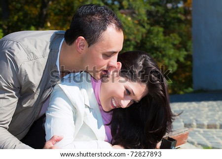young man giving a kiss her ear, happy couple standing outside on a sunny day