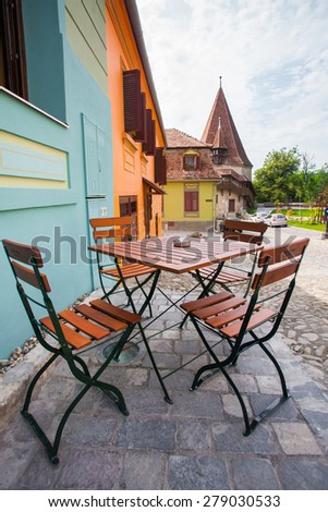 Sighisoara, Romania - June 23, 2013: Table with chairs on stone paved old street and colored houses from Sighisoara fortress, Romania