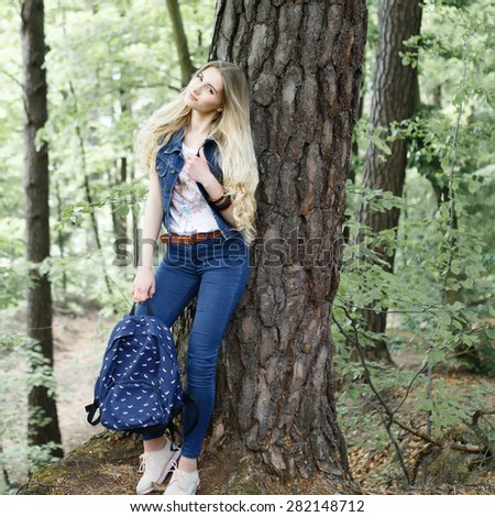 Young blonde girl hipster forest hike with a backpack in jeans