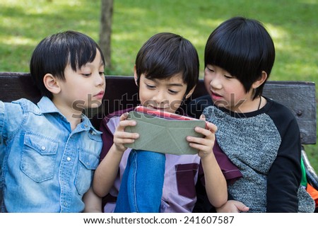 Three Little handsome boy looking on ipad tablet and playing game at park