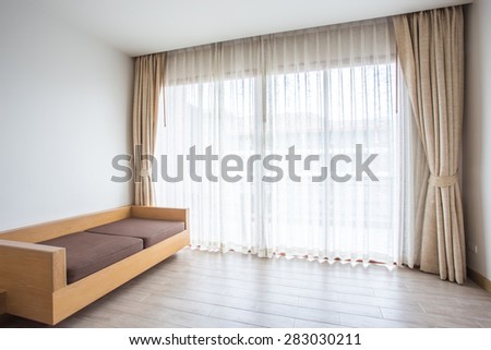 Light shines through white curtains in room with wooden sofa