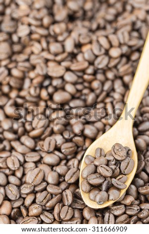 coffee beans in spoon on roasted coffee seed background