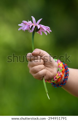 child hand in rubber band bracelets with flower on blurred background