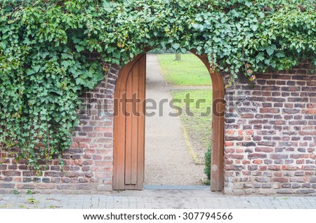 An entrance gate in a wall into a park. Behind the open door is a way.