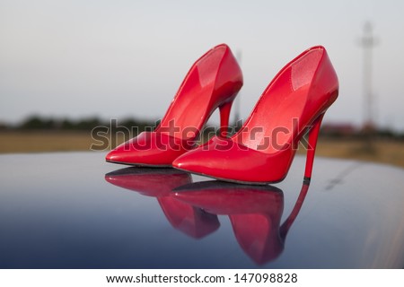 A pair of red high heel shoes on top of a blue car with reflection
