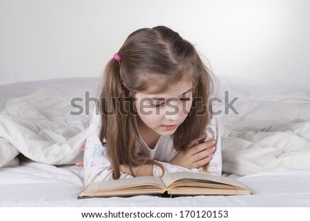 Little girl lying in bad and reading the bible written in Hebrew