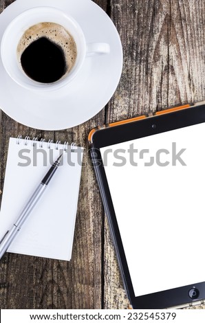 Morning coffee with a spiral notepad and fountain-pen and a tablet on old brown dood background