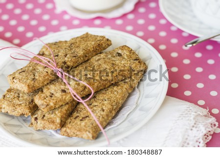 Oatmeal and linen integral cookies on white and pink polka dots tablecloth, prepared with a cup of coffee and some milk, ready for breakfast.