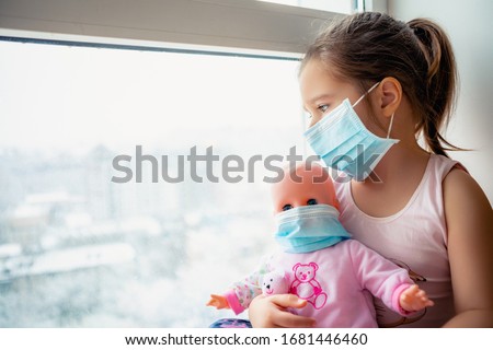 Little girl in hospital. Child girl with doll wearing a protective mask. Copy space. Sadness kid at home in isolation. Sick child   Little girls look at the window with longing          