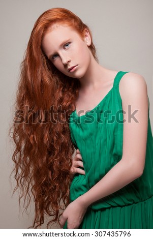 Beautiful teen model in a green dress and long red hair, tilted her head to the side hair hang down