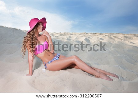 slim tanned girl in a bathing suit on the beach  looking  in profile, in a pink hat with long legs