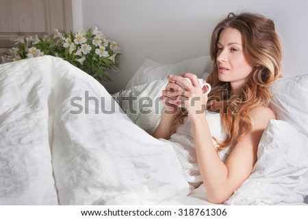 Morning awakening from the scent of fresh flowers and a cup of tea in bed. Warm and comfortable bed, a beautiful blond woman lying in bed, brown eyes and curly hair on her face. Concept Morning.