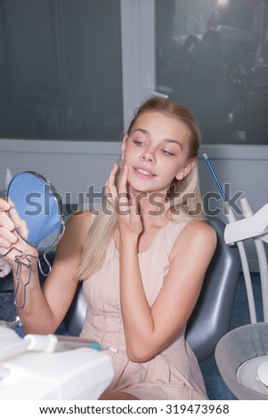 The girl at the dentist. Dentist holds the tools, limited to users sitting in an armchair at the doctor. A beautiful woman looks in the mirror sitting in a chair with a dentist, beautiful white teeth