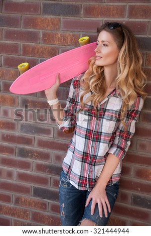 The girls on skateboards. Slim and beautiful woman holding a pink skate. Attractive girl in jeans and shirt holds the skate. Stylish girl goes in for sports and fun riding on a skateboard