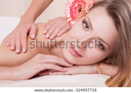 Beautiful woman in dark hair and a flower in her hair,girl do massage of the back, she looks into the camera.A woman with light make-up on her face in a spa salon.Massage the back for a beautiful girl