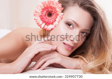 Portrait of a beautiful woman with brown eyes and perfect skin on her face in her hair pink flower,she looks straight into the camera lying on his stomach.Girl in a beauty salon,her hand near the face