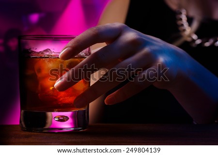 Woman\'s hand holding old fashioned glass with cold cocktail against blurred night club background