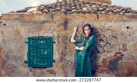 Beautiful women wearing traditional greek green colored dress posing while leaning on scrawled wall. Instagram filter styled.