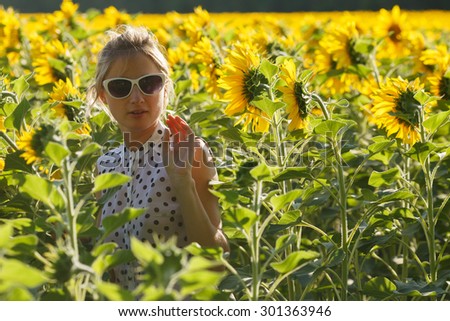 Eccentric woman wearing sunglasses, black and white polka dot dress fooling around in the sunflower field. Selective focus,natural light, backlit,flare