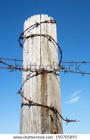 Barbed wire fence post against a blue sky