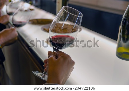 Some people are holding red wine cups in a wine tasting to see the wine transparency