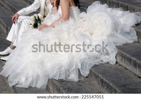 detail of a bride\'s dress seated on the ground with her groom