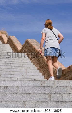 An adult woman wearing miniskirt walks up the stairs with an smartphone