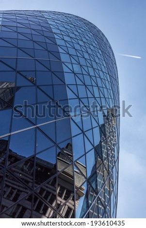 CENTRAL LONDON / ENGLAND - 18.05.2014 - Sky-scraper reflections are seen in the Gherkin\'s windows while a plane flies over London.