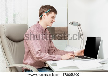 Horizontal portrait of young man sitting behind desk with laptop and typing text