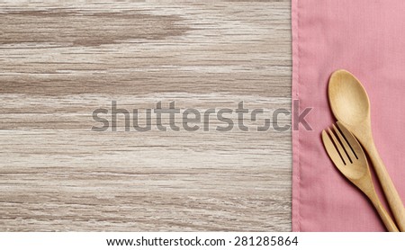 Wooden spoon and fork on pink towel and wood board background