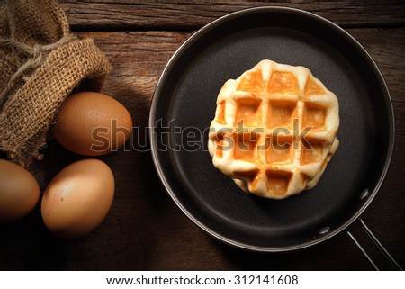 Baked waffles inside the teflon pan and eggs on wood background