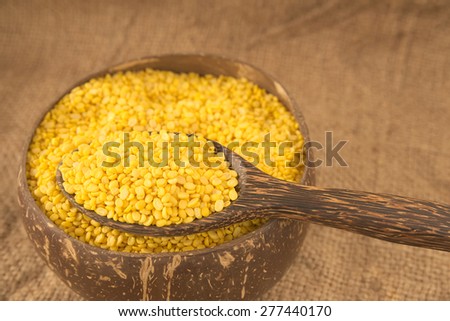 Spoonful of peeled green bean on a bowl filled with peeled green beans over agriculture sack background