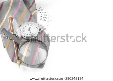 Expensive pen, pocket watch, royal flush cards, and magnifier glass on top of vibrant strip color gray necktie with royal flush cards over white background