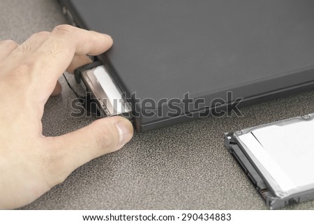 Male hand pulling out HDD out of black laptop slot over working desk with another HDD in front of laptop