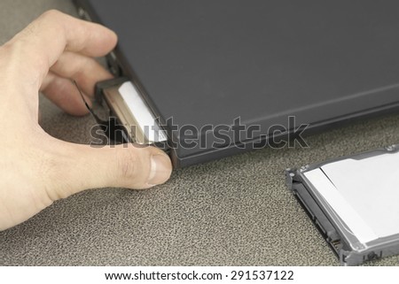Male hand pulling out HDD out of black laptop slot over working desk with another HDD in front of laptop