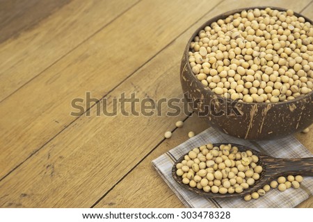 Abstract copyspace of wooden bowl filled with full size yellow beans and a spoonful of bean over napkin on top of wooden table