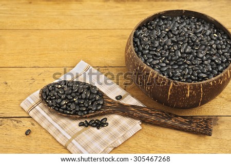 Bowl fully filled with black bean and a spoonful of black bean on napkin over wooden table.