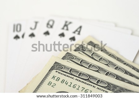 Highest possible hand in poker, royal flush, over white background with pile of dollar note on top.