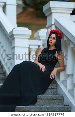 Beautiful black haired woman with red flower chaplet are waiting at the stairs